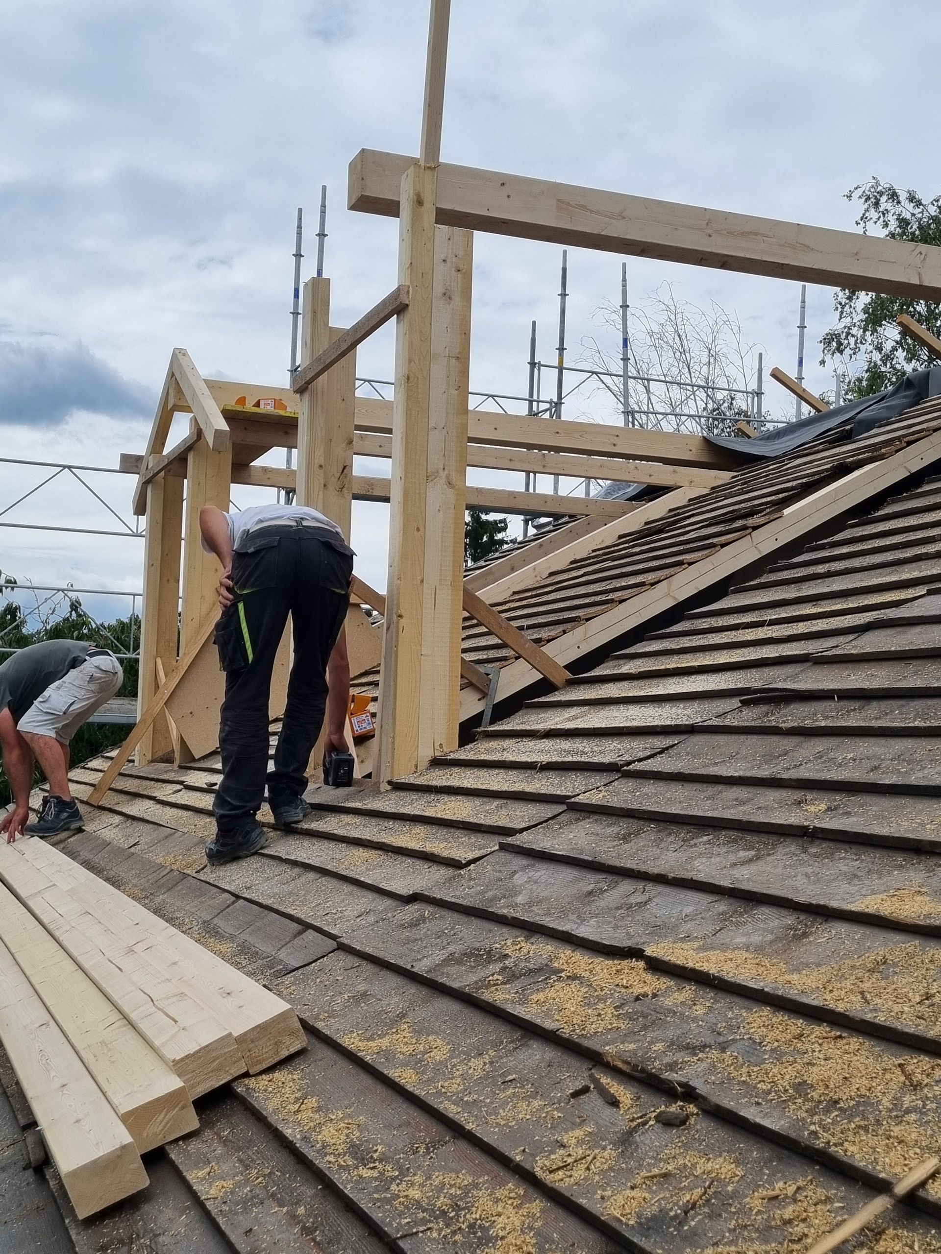 Deux ouvriers du bâtiment construisent une nouvelle charpente de toit en bois sur un toit de tuiles existant.