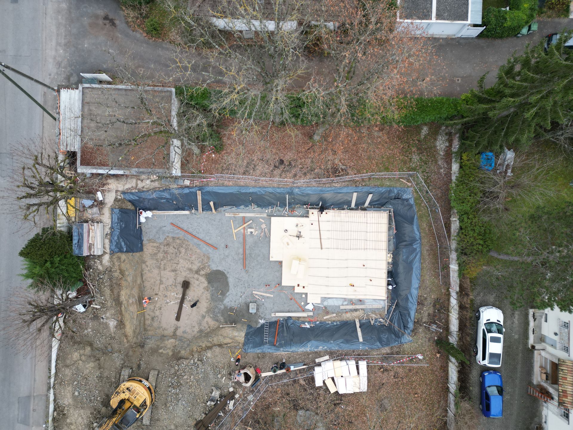 Vue aérienne d'un chantier de construction résidentielle montrant une excavation de fondation revêtue de plastique et partiellement isolée.