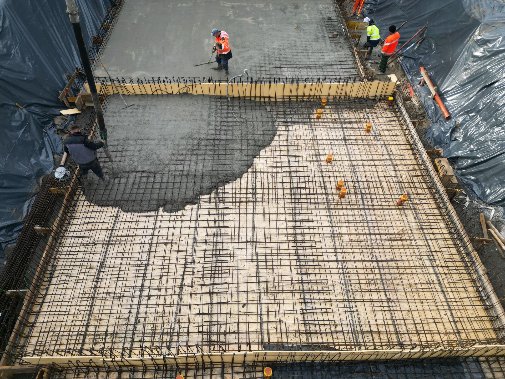 Des ouvriers du bâtiment coulent du béton sur une fondation en treillis d'armatures métalliques dans un grand chantier de fouilles.