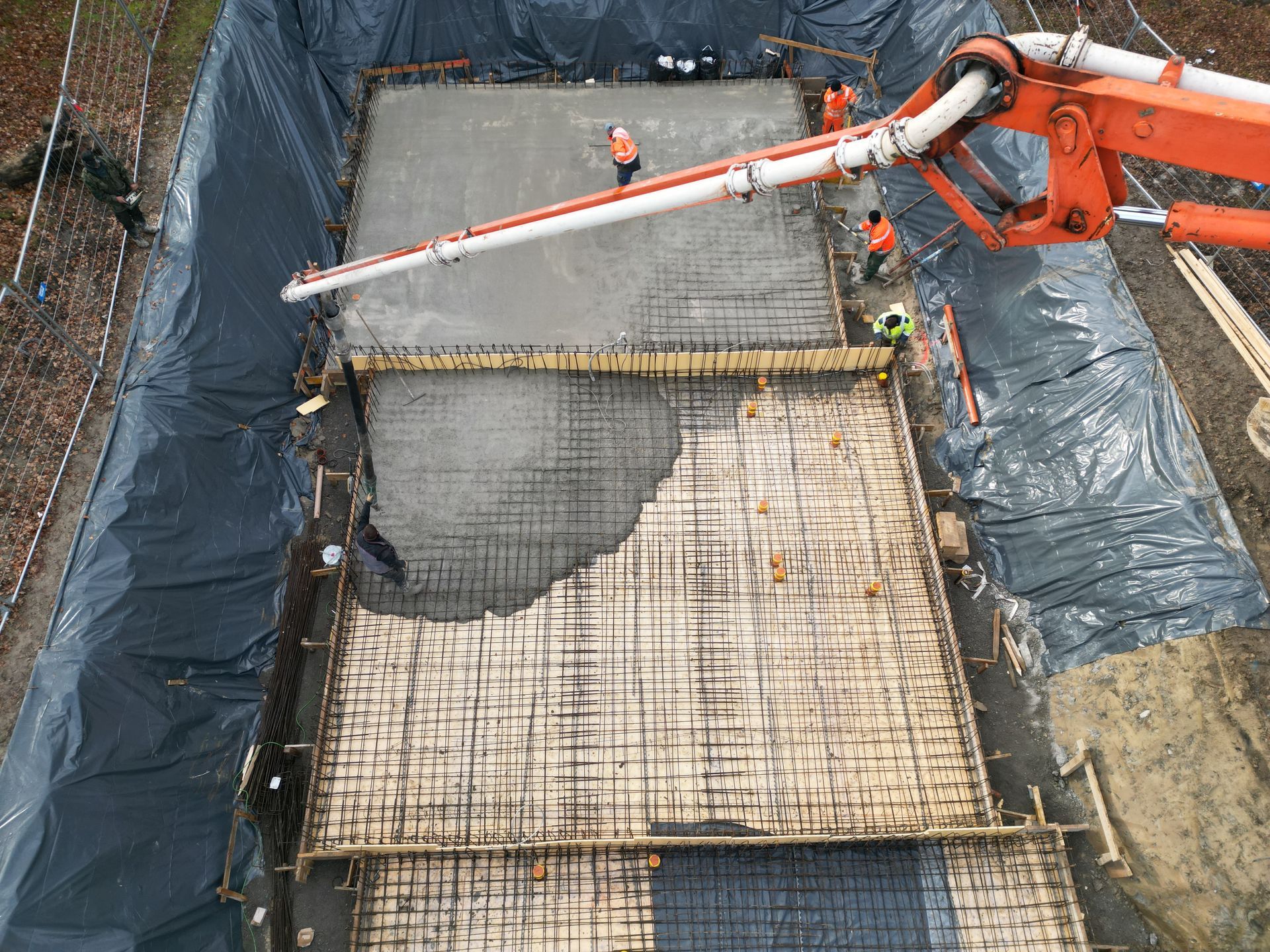 Vue aérienne d'un camion-pompe à béton déversant du béton frais sur une fondation renforcée d'armatures métalliques à l'intérieur d'une tranchée revêtue.