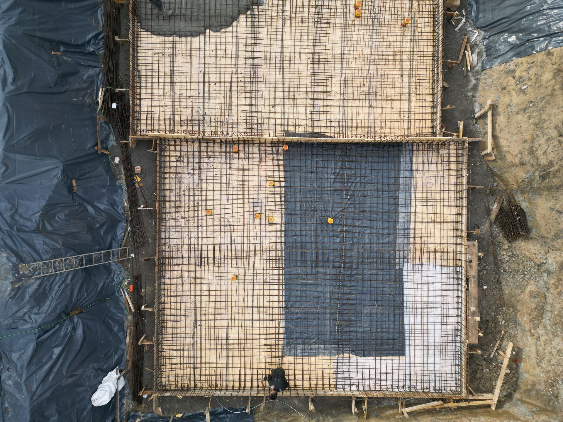 Vue aérienne d'un chantier de construction rectangulaire montrant les grilles d'armatures métalliques préparées pour le coulage d'une fondation en béton.