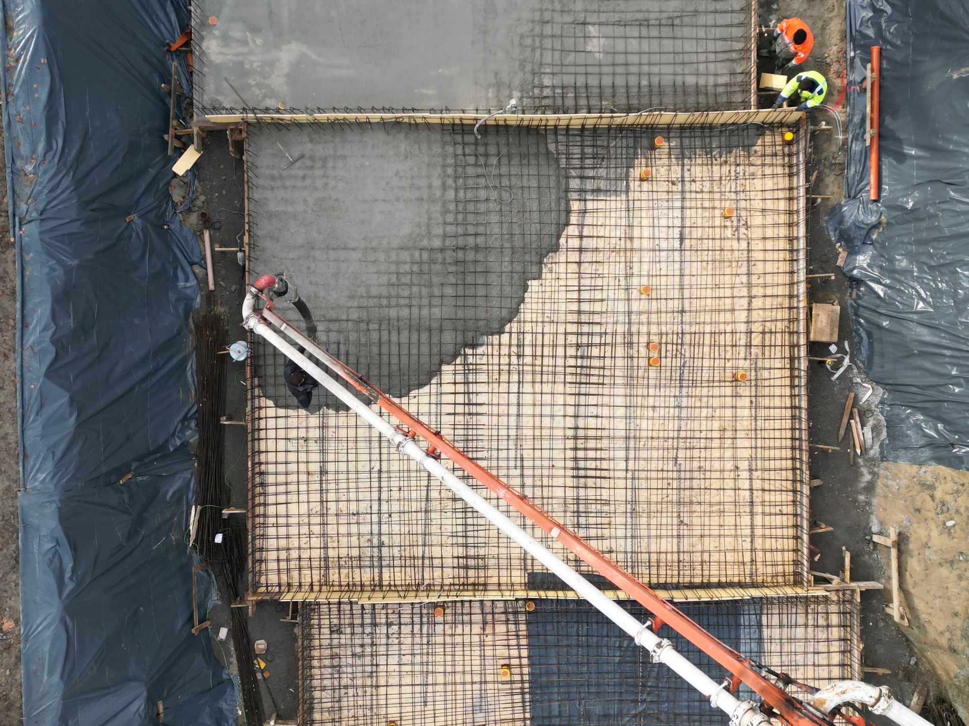 Vue aérienne d'un coulage de béton sur une dalle rectangulaire armée, remplie par la flèche d'une grande pompe à béton.