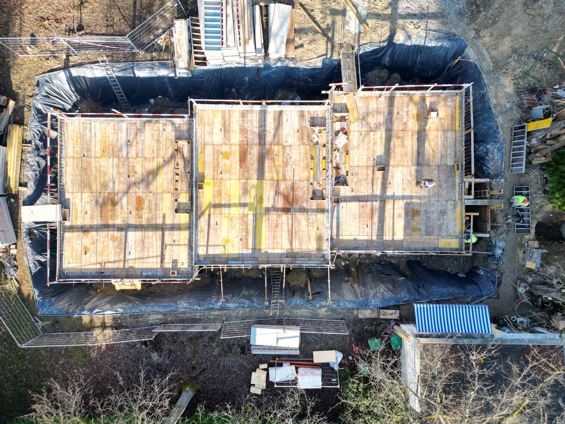 Vue aérienne d'un chantier de construction de fondations résidentielles montrant un coffrage en bois et des semelles en béton dans une fosse de terre.
