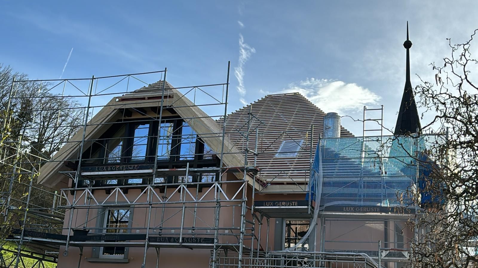 Une maison couleur pêche, au toit de tuiles, en construction, entourée d'échafaudages et dotée d'une tourelle proéminente.