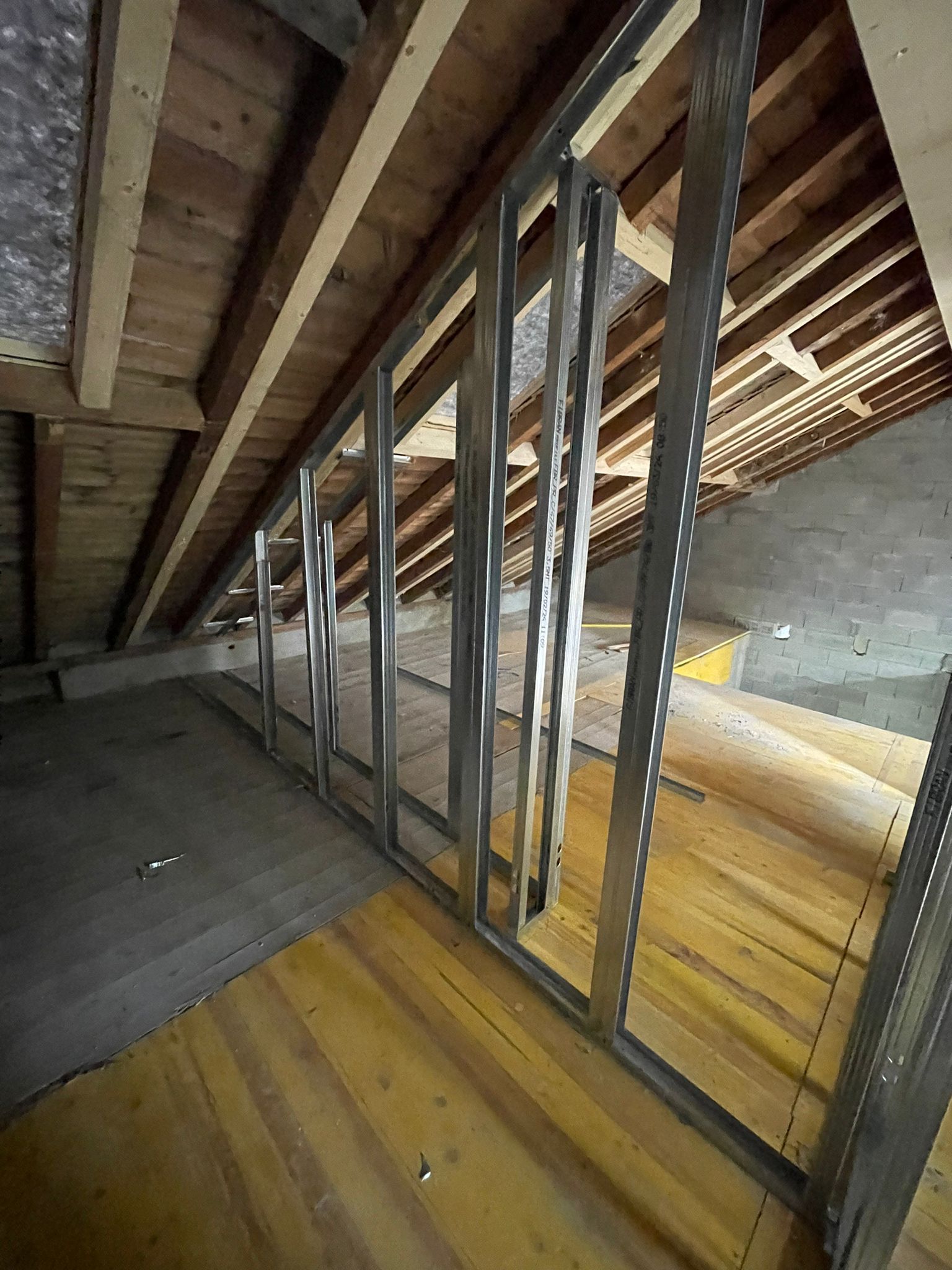 Une ossature métallique en construction dans un grenier avec des chevrons et un plancher en bois.