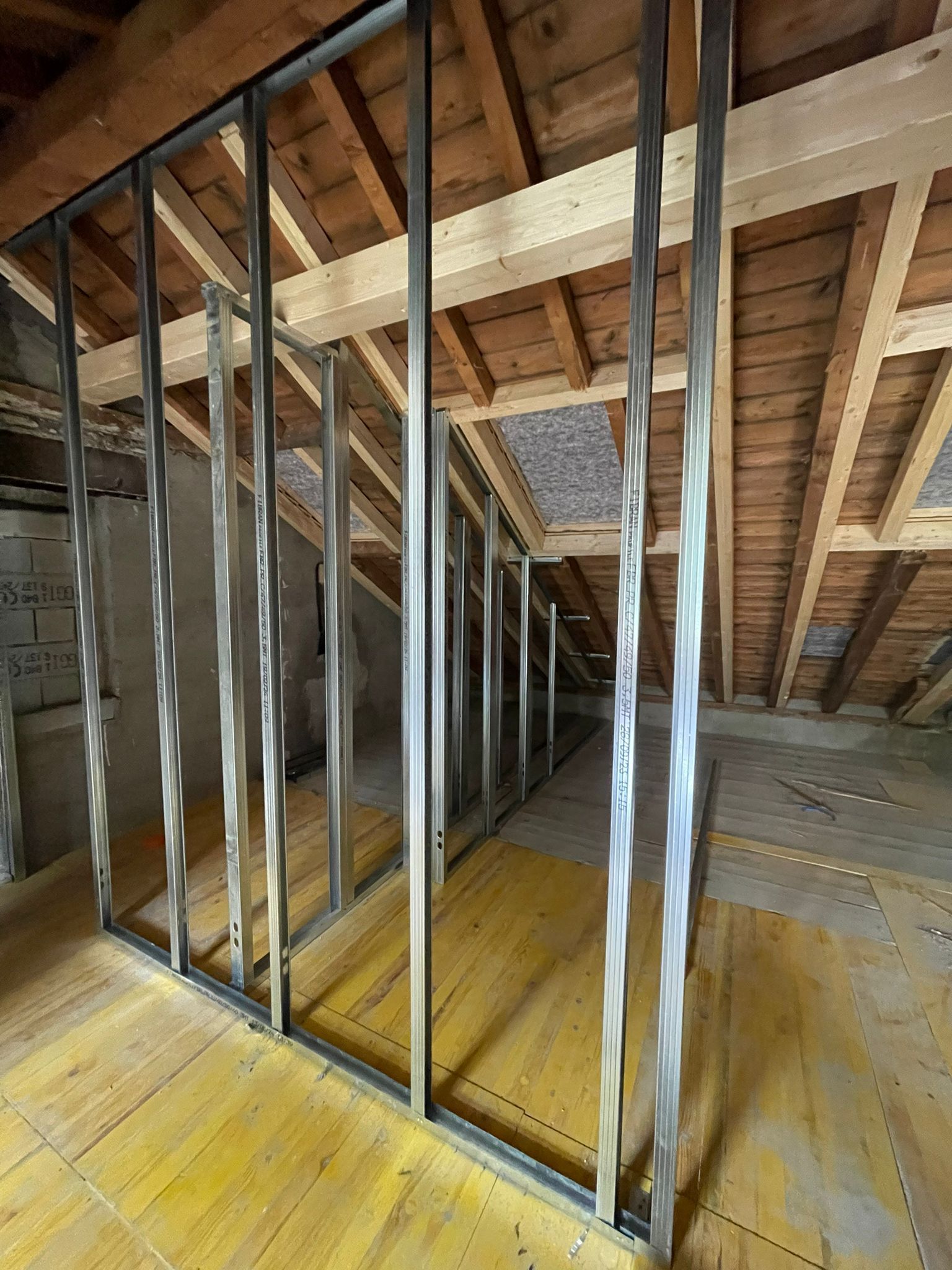 Une ossature métallique murale installée dans un grenier avec des chevrons en bois et un plancher en contreplaqué.