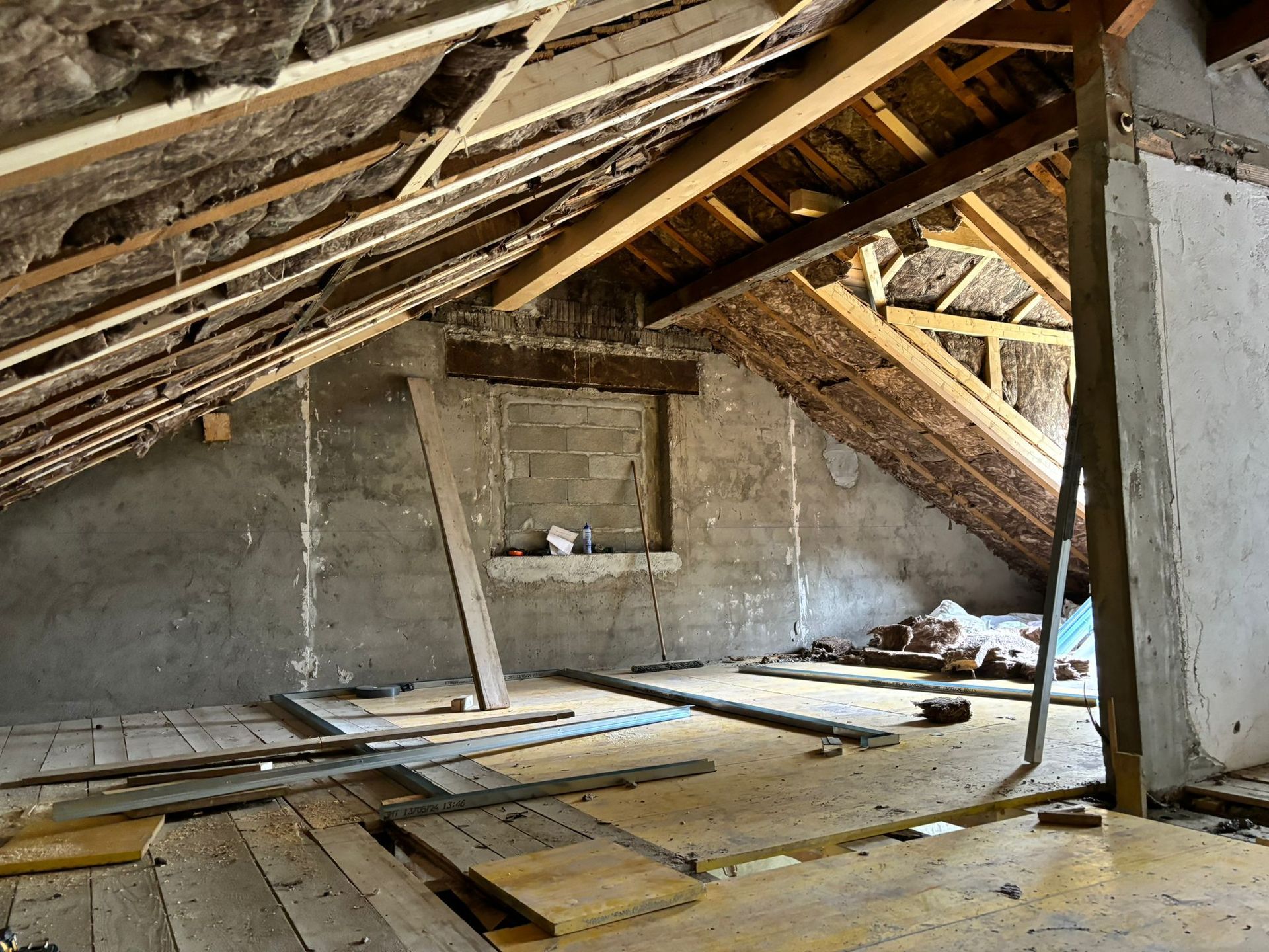 Un grenier inachevé, aux murs nus, en cours de rénovation, avec poutres de toit et plancher en bois apparents.