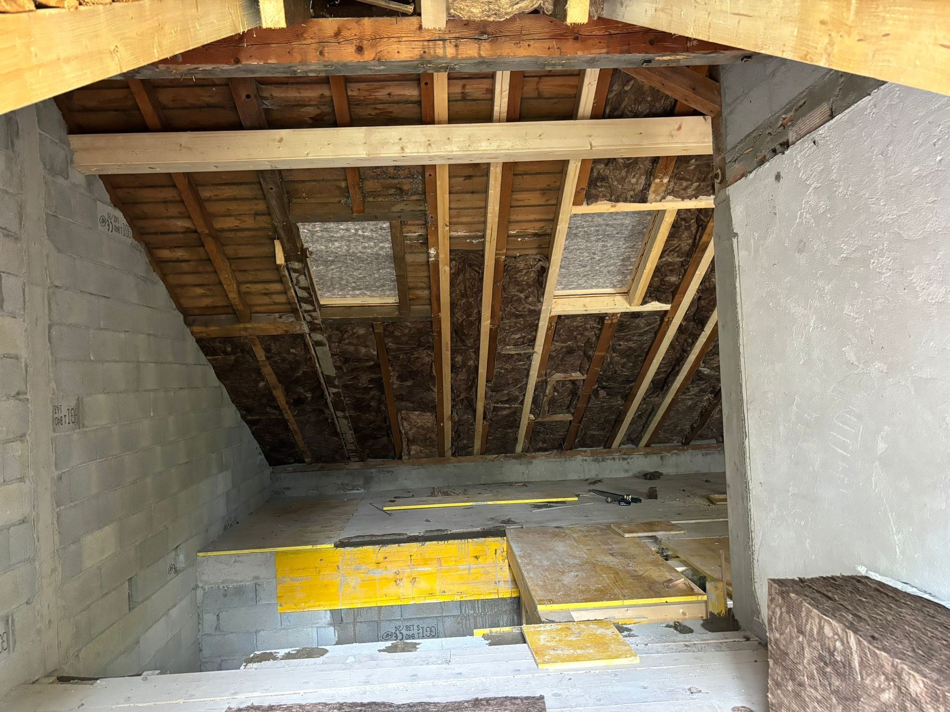 Intérieur du grenier non aménagé avec charpente apparente, isolation, deux puits de lumière et plancher en contreplaqué.