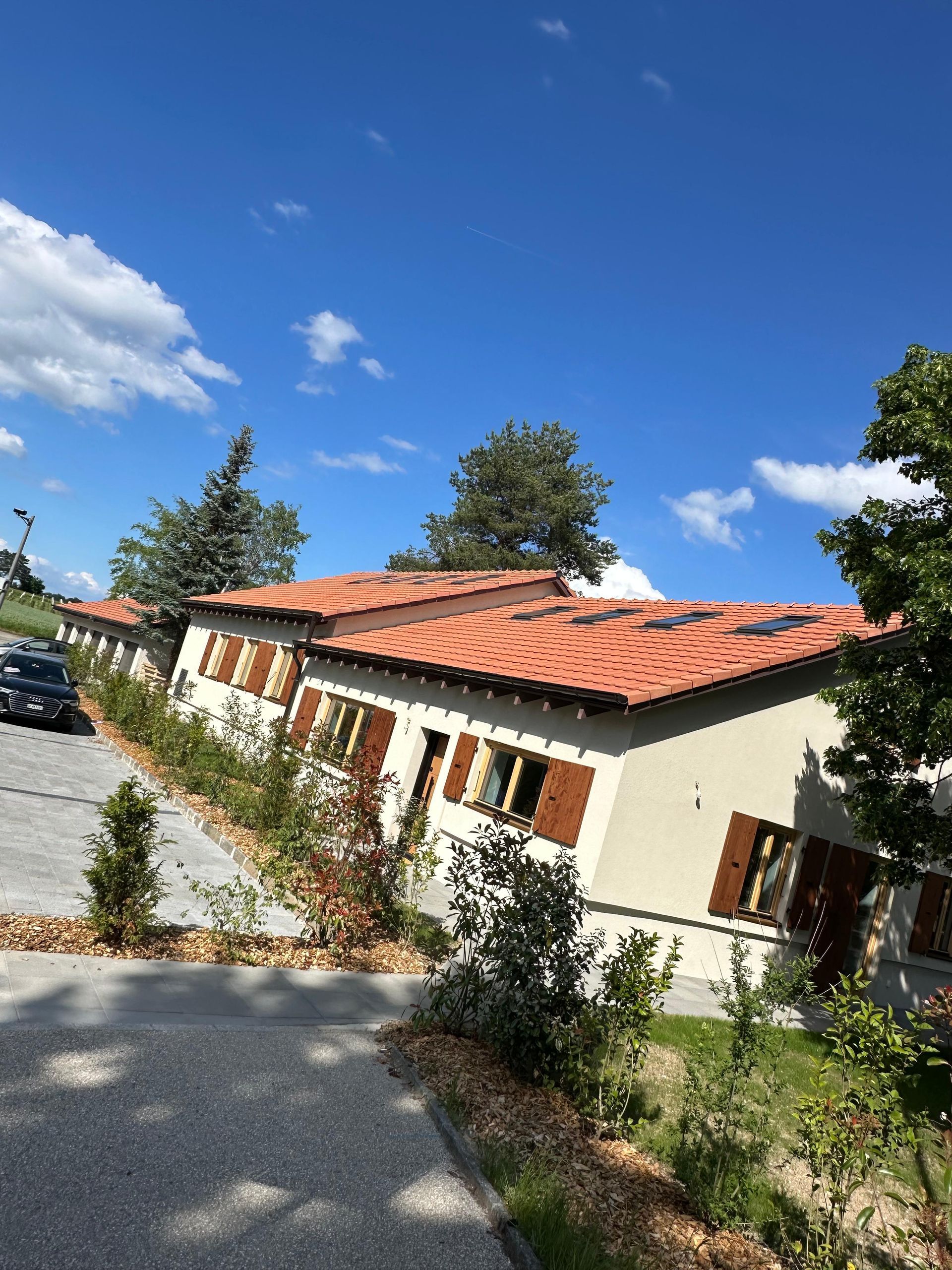 Une rangée de bâtiments de plain-pied aux toits de tuiles orange, aux murs clairs et aux volets bruns, sous un ciel d'un bleu éclatant.