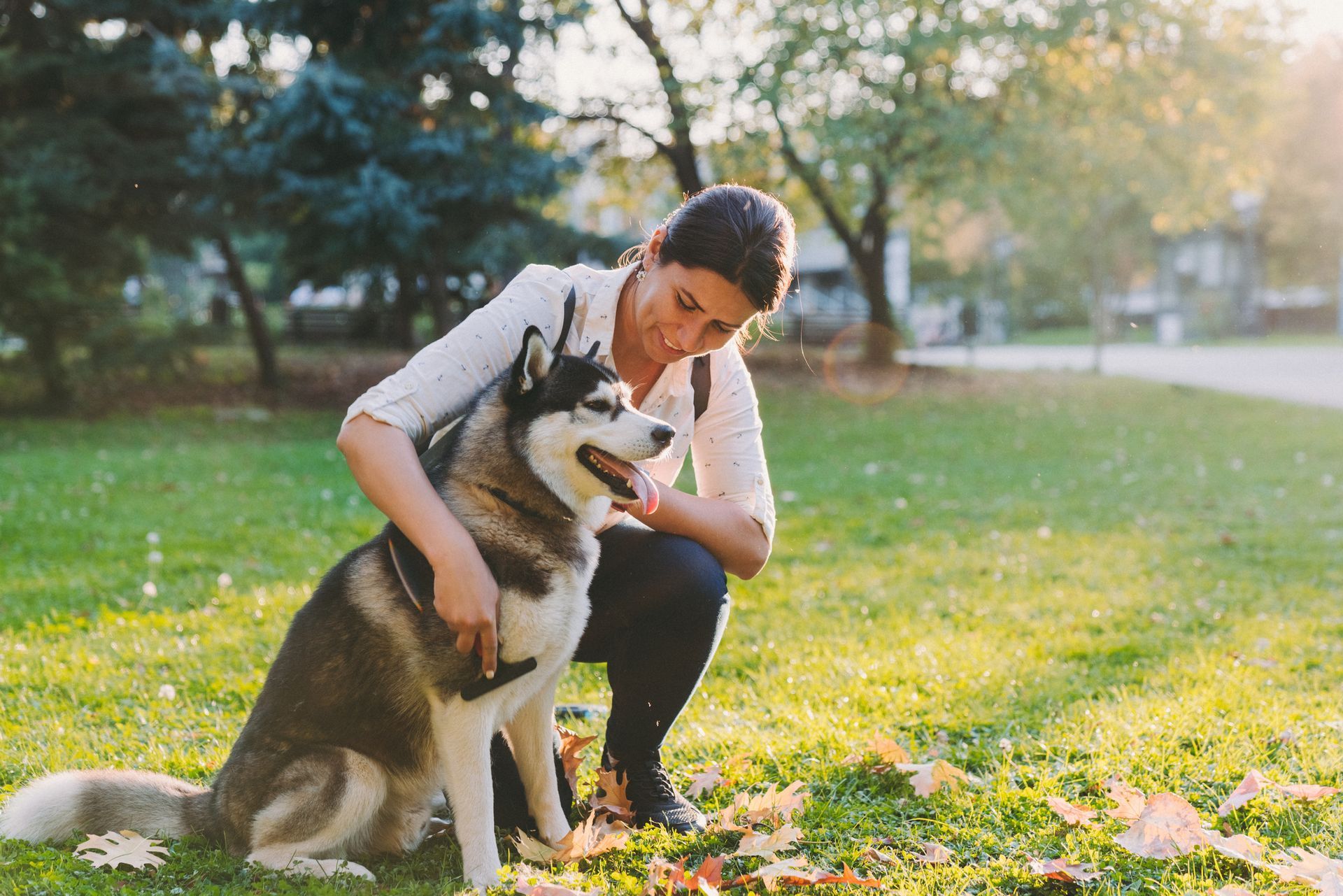 A woman is kneeling down next to a husky dog in a park.