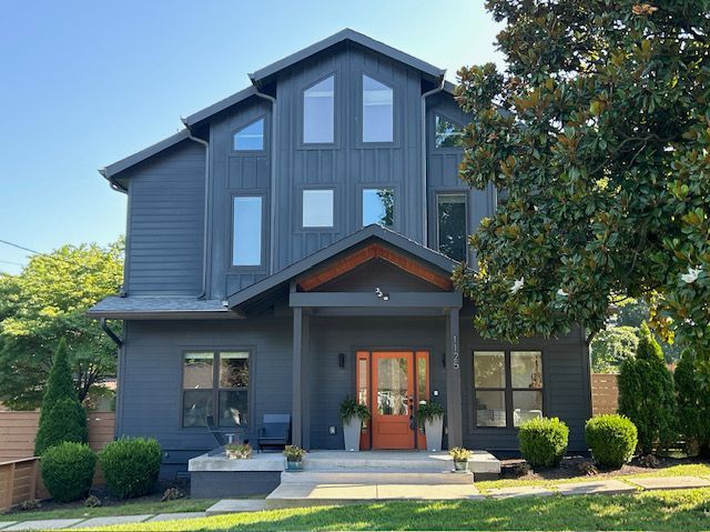Modern, three-story gray house with orange front door, porch, and landscaping.