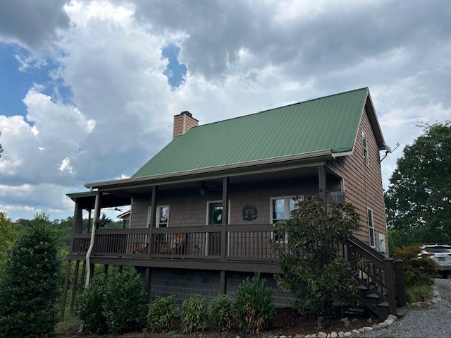 Brown cabin with green roof under a cloudy sky.