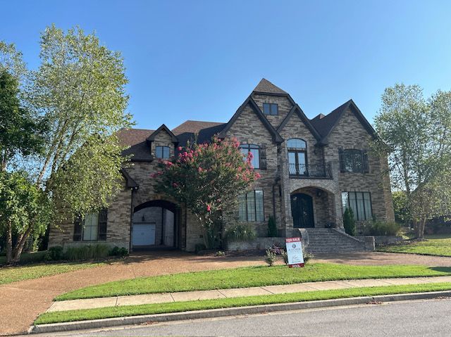 Large brick house with multiple gables and arched entry under a clear blue sky.