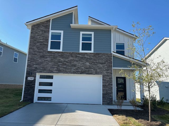 Modern two-story house with blue siding, gray stone accents, and a white garage door against a blue sky.