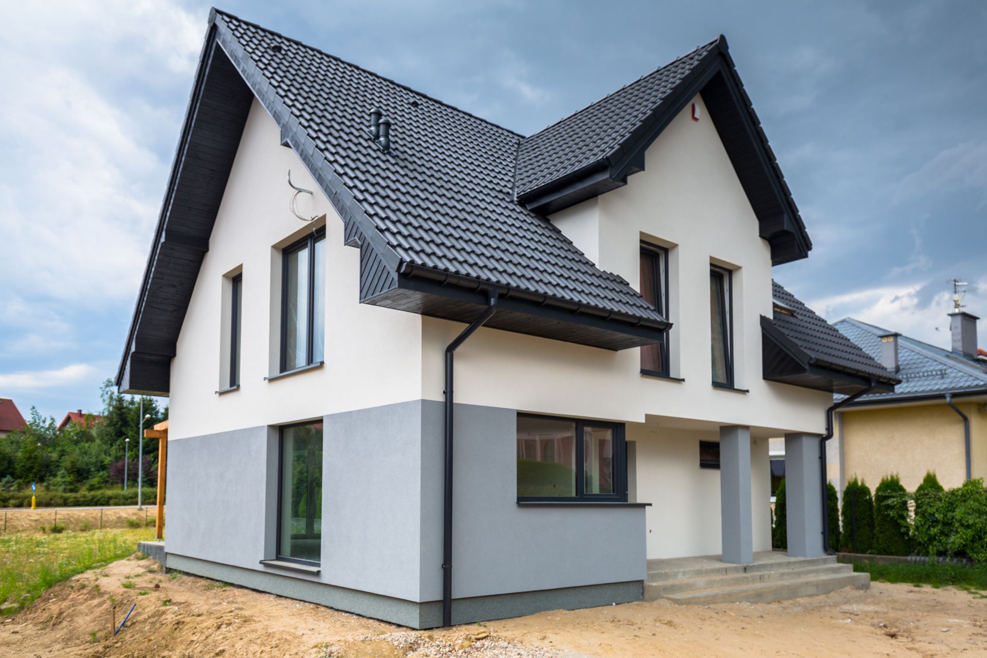 Two-story house with white and gray exterior, black roof, and windows, under a cloudy sky.