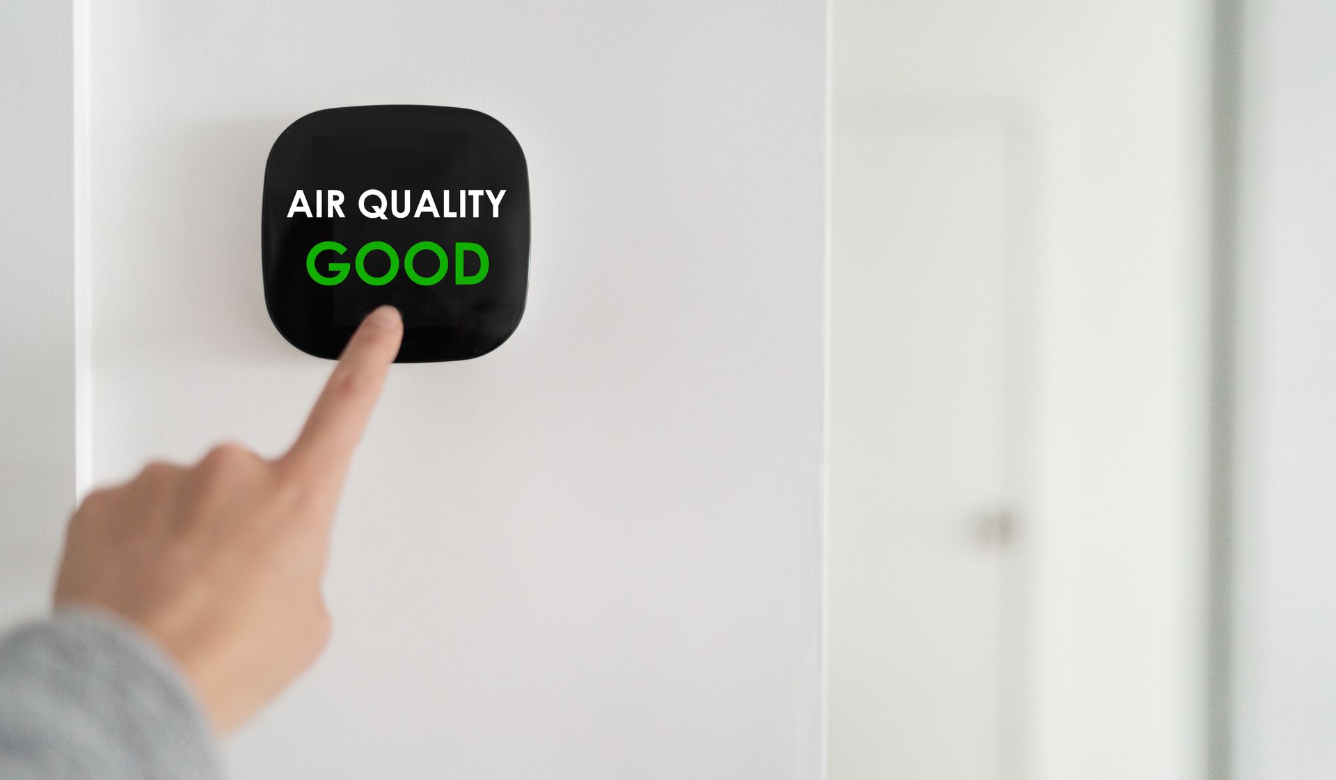 A person's finger pointing at an air quality monitor displaying 