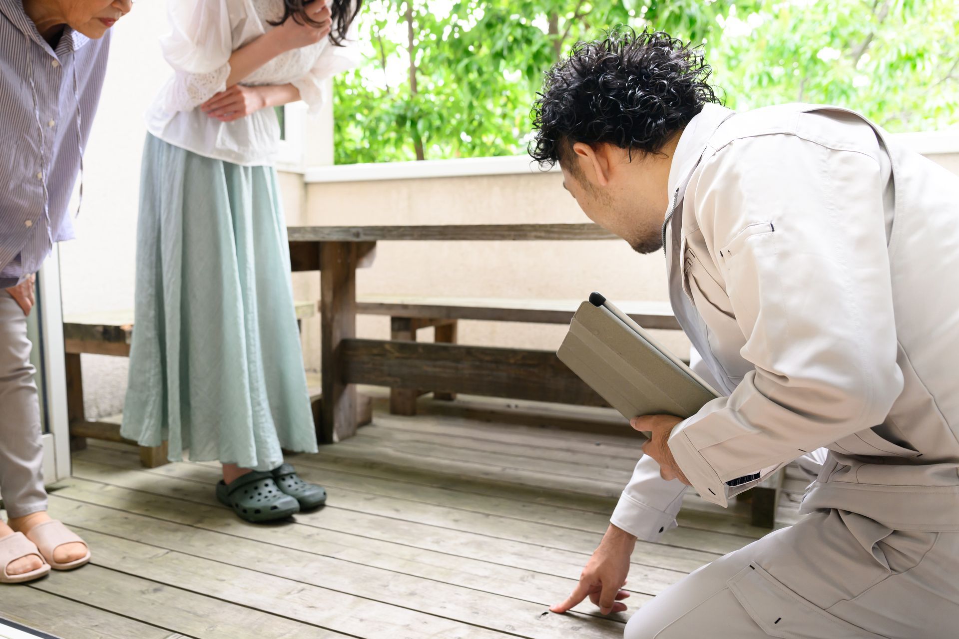 A person in work clothes kneels on a wooden deck, pointing, as two others observe.