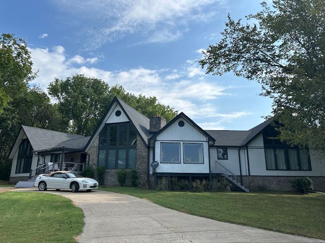 White car parked on a driveway in front of a modern house with black trim and a blue sky.