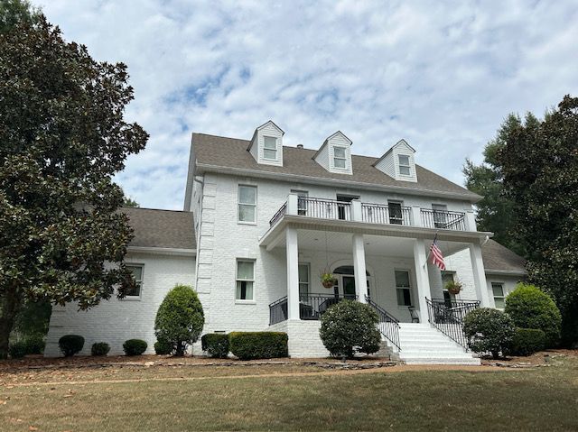 White two-story house with front porch and dormers, set on a grassy lawn.