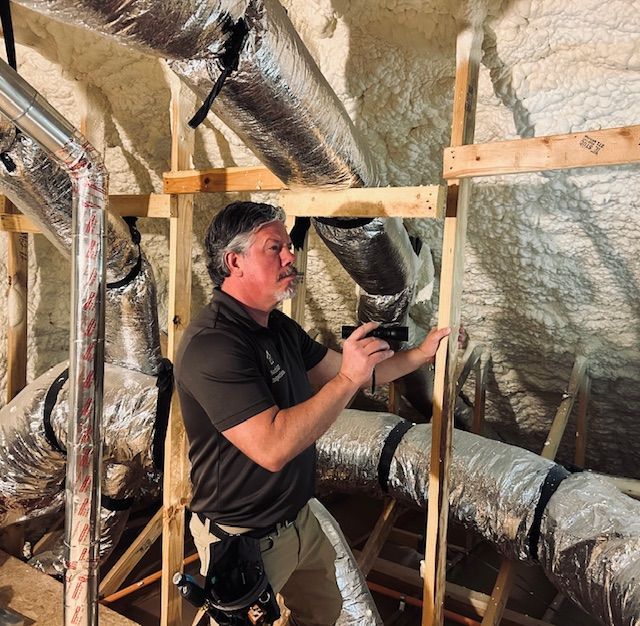 Man inspecting framing in an attic space. Silver ductwork and insulation present.