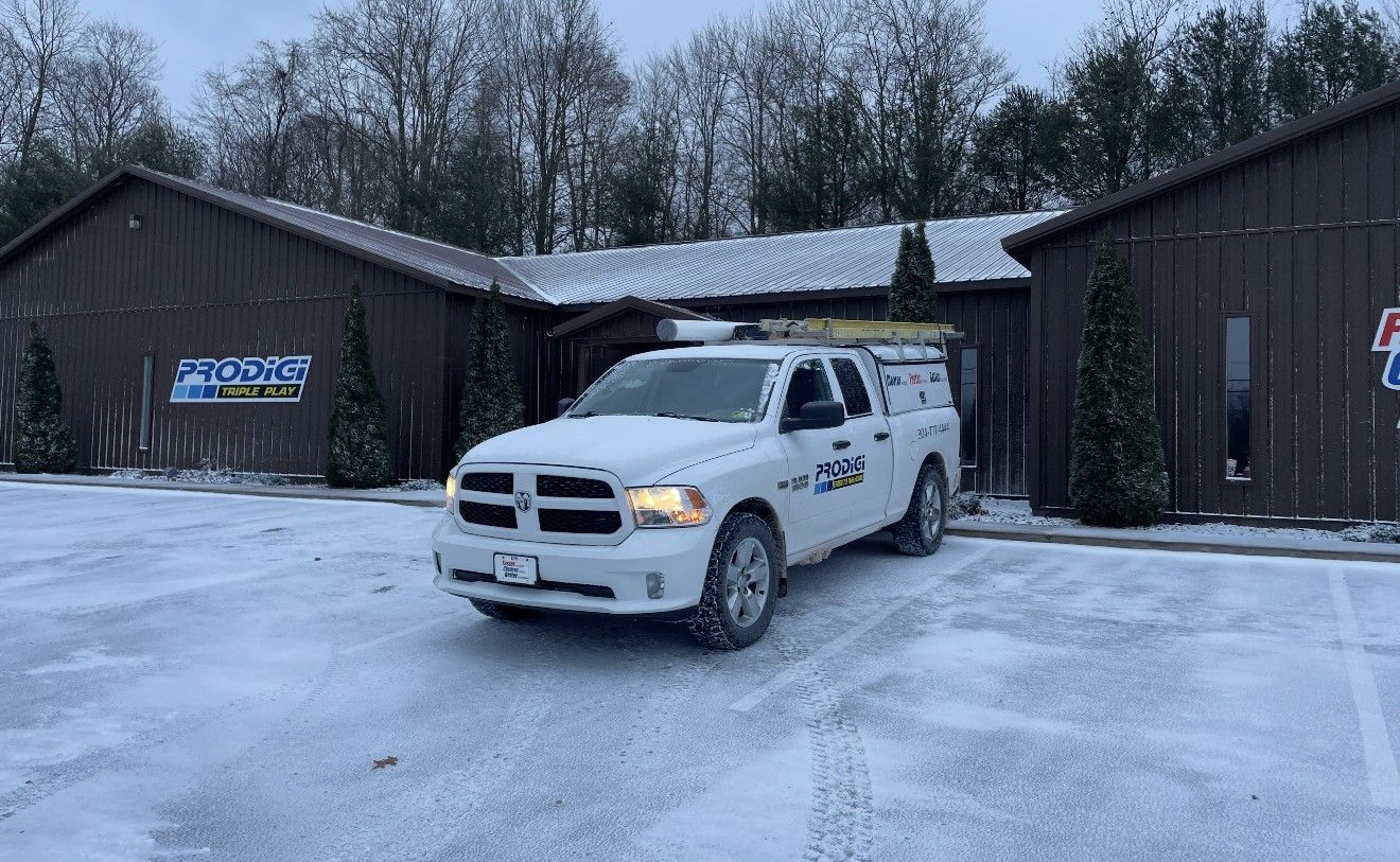 A white pickup truck with logo branding is parked in a snowy parking lot in front of a dark, barn-style commercial building.