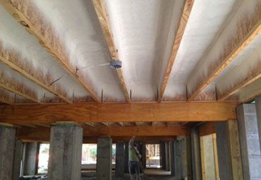 A man is spraying foam on the ceiling of a building under construction.
