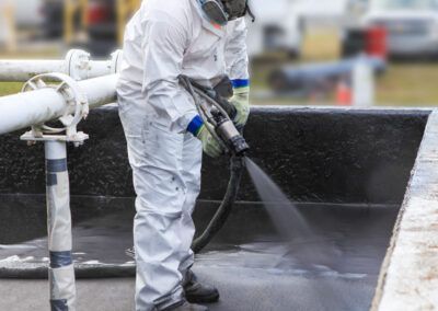 A man in a protective suit is spraying a black surface.