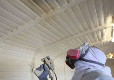A person is spraying foam on the ceiling of a building.