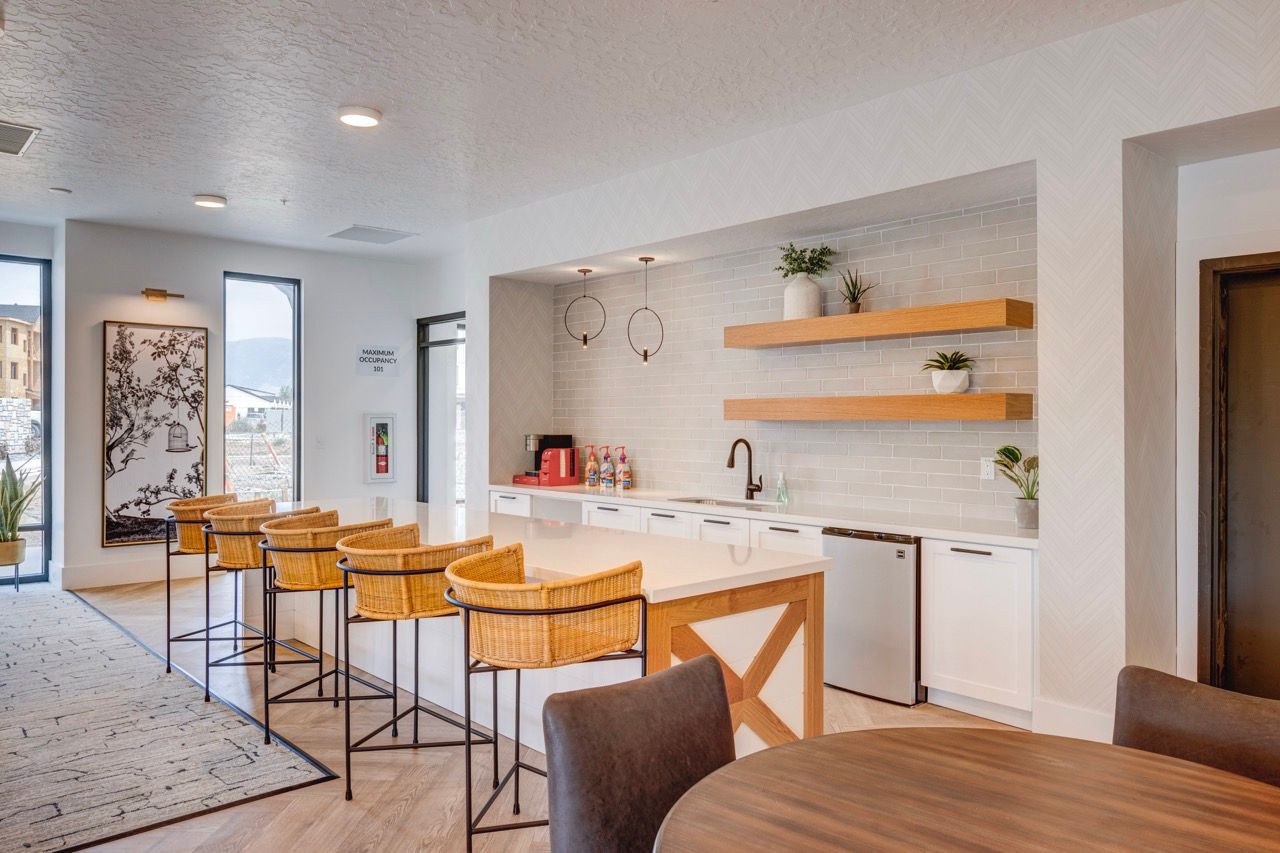 Aria communal kitchen area with white cabinets, a large island, wicker bar stools, and wooden shelves.