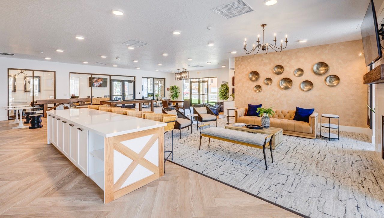 Bright community lounge with beige couches, chairs, a long white island, and wall decor.