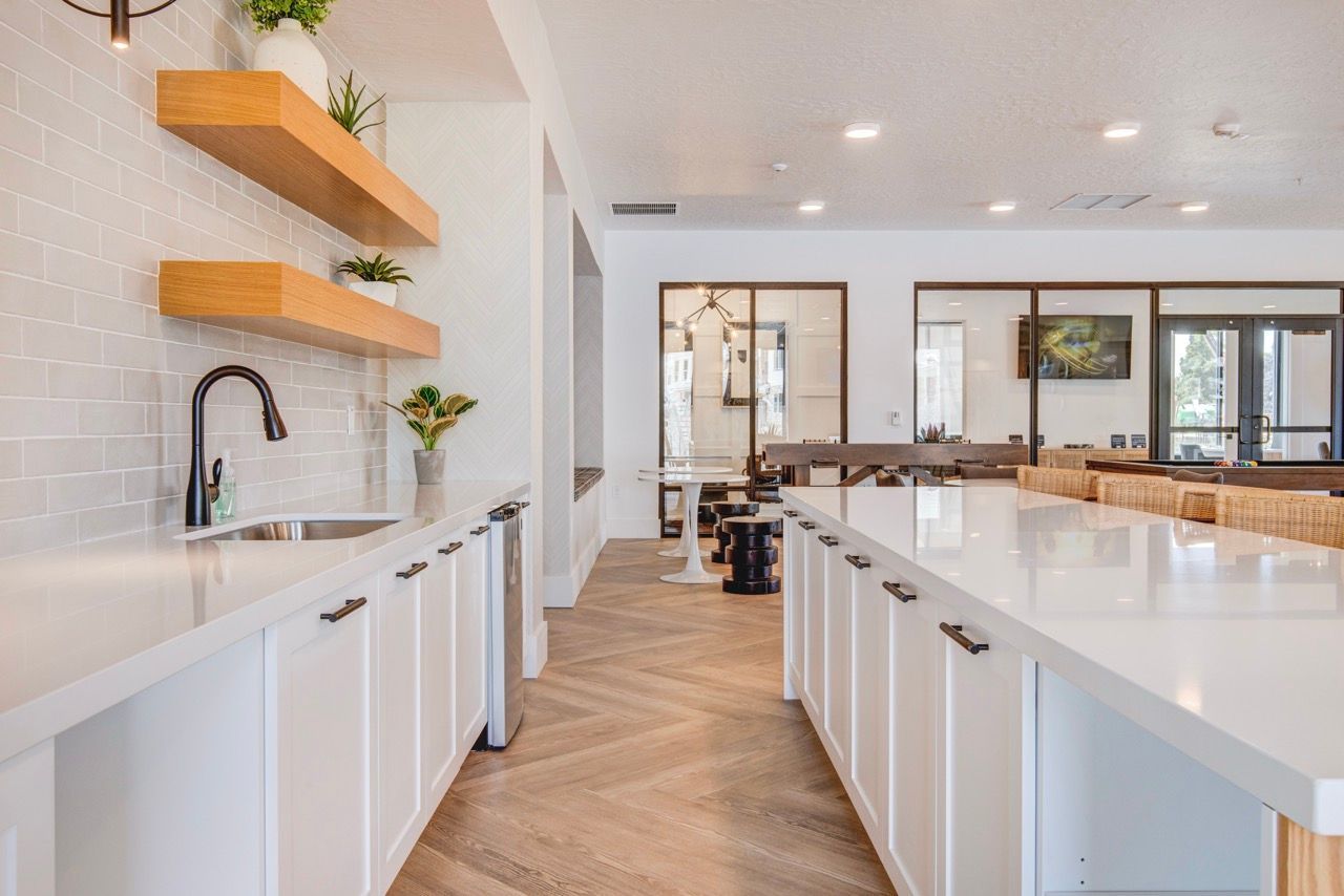 Aria communal kitchen with white countertops, sink, and floating wooden shelves.