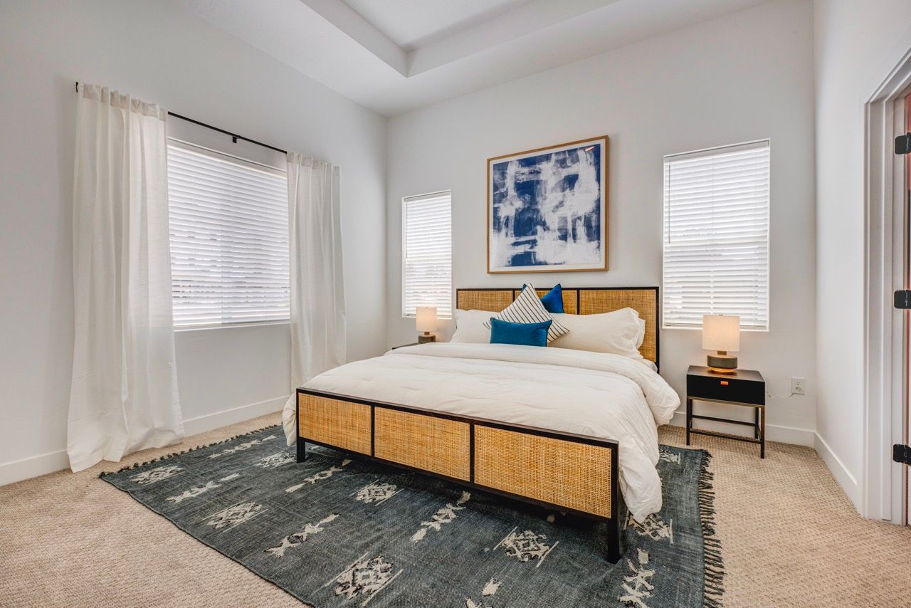 Aria Bedroom in a modern apartment with a bed, nightstands, lamps, and large windows with blinds.