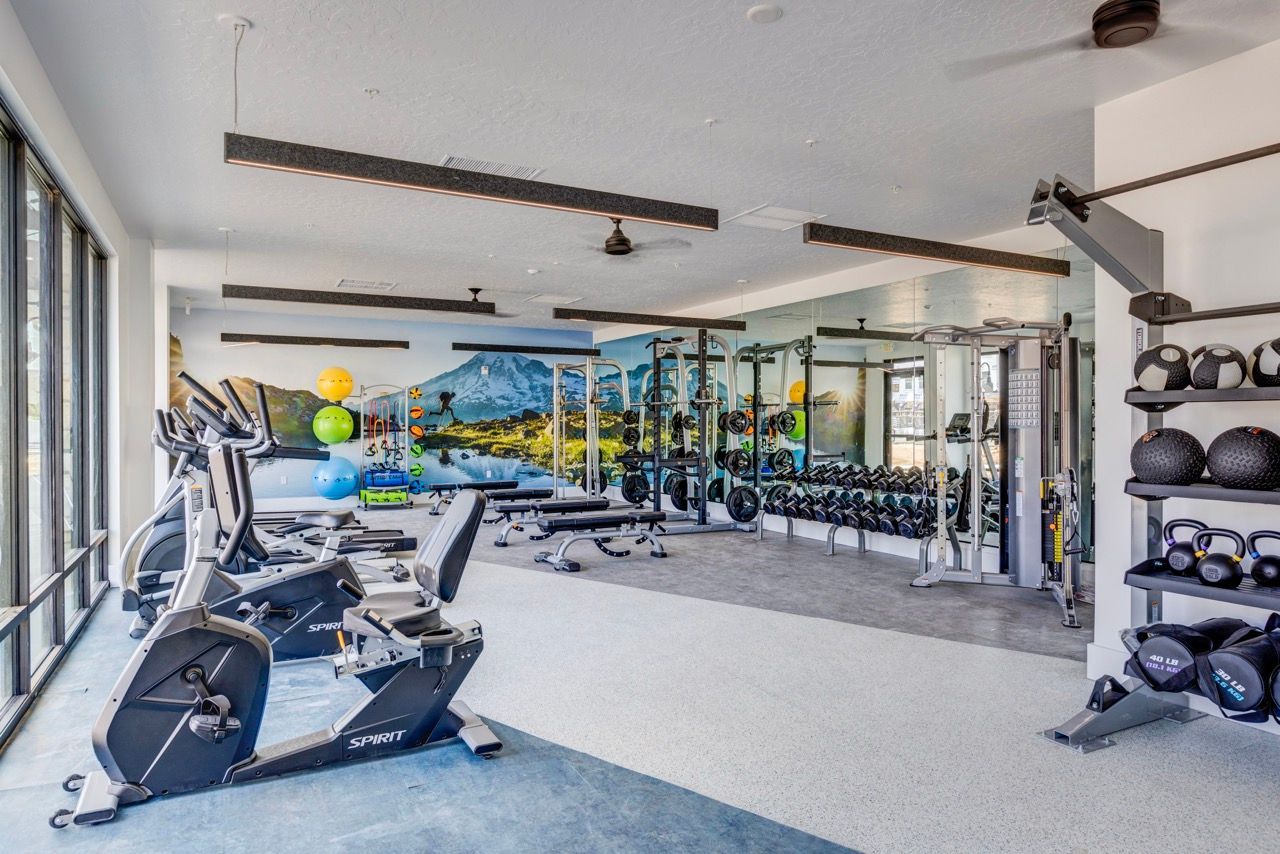 Bright on-site fitness center with cardio machines, free weights, and a wall mural.