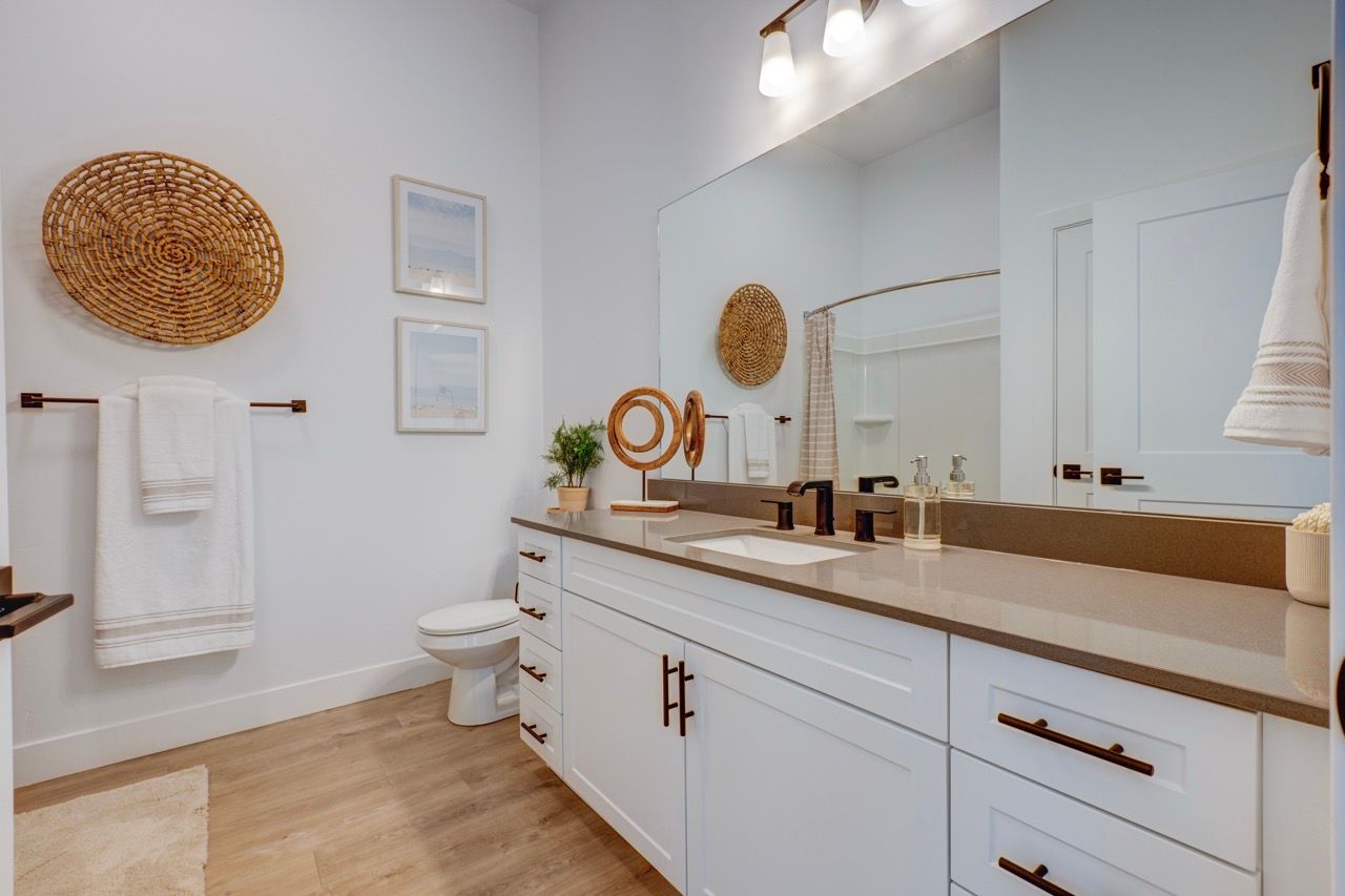 Aria bathroom with white vanity, beige countertop, large mirror, towel rack, and toilet.