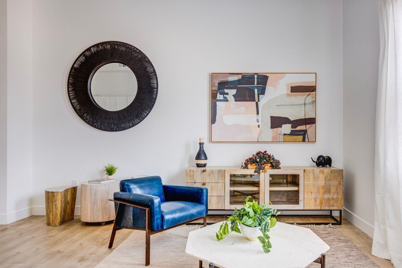 Aria Living room in a modern apartment with a blue armchair, round black mirror, and abstract art.