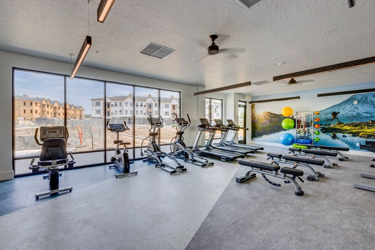 Aria community gym with treadmills and stationary bikes, large windows, and a mural on the wall.