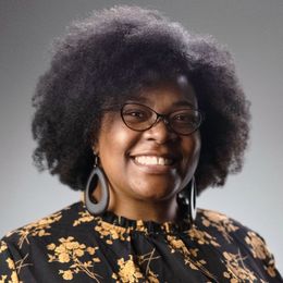 a woman wearing glasses and earrings is smiling for the camera .