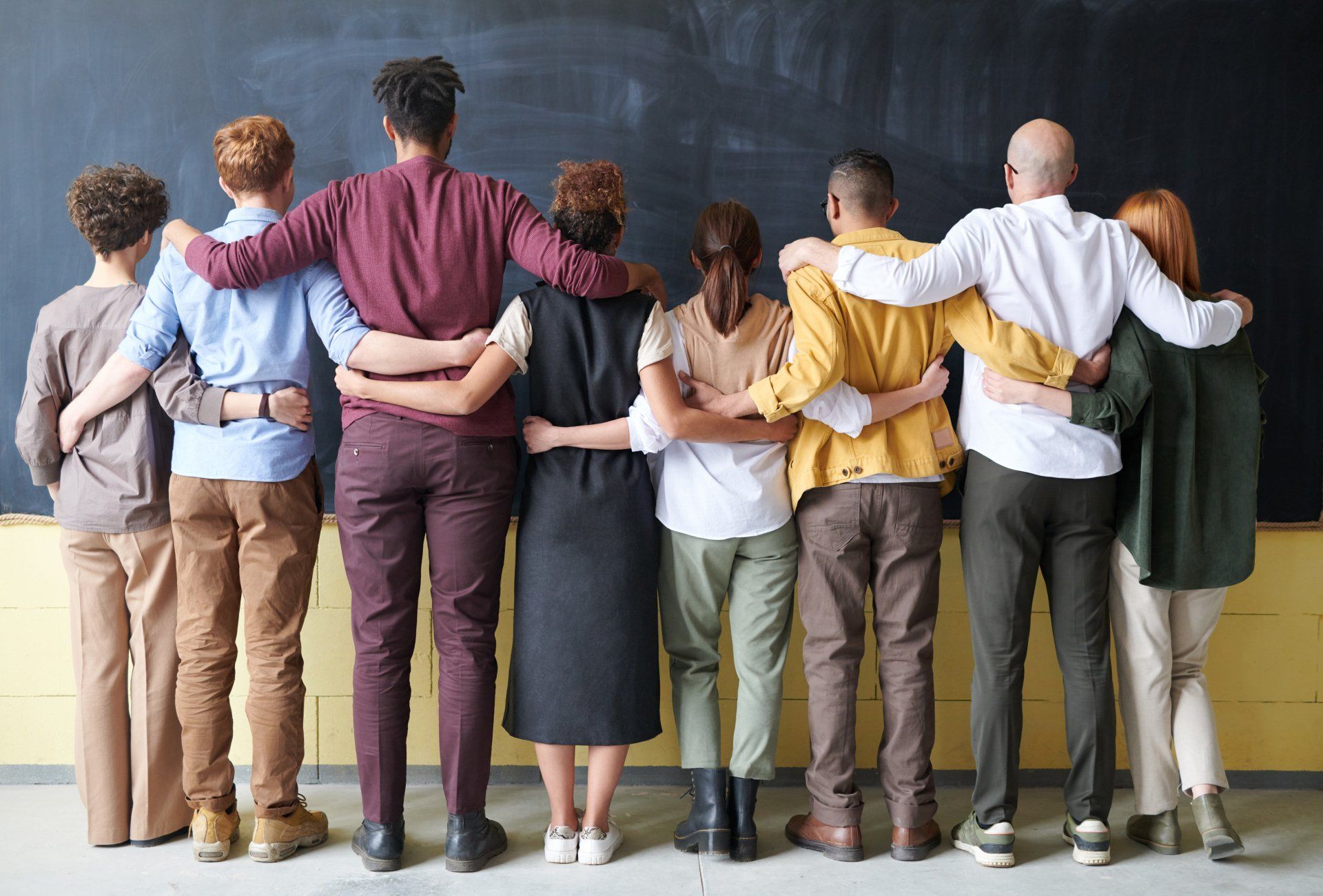 A group of people are standing in front of a blackboard with their arms around each other.