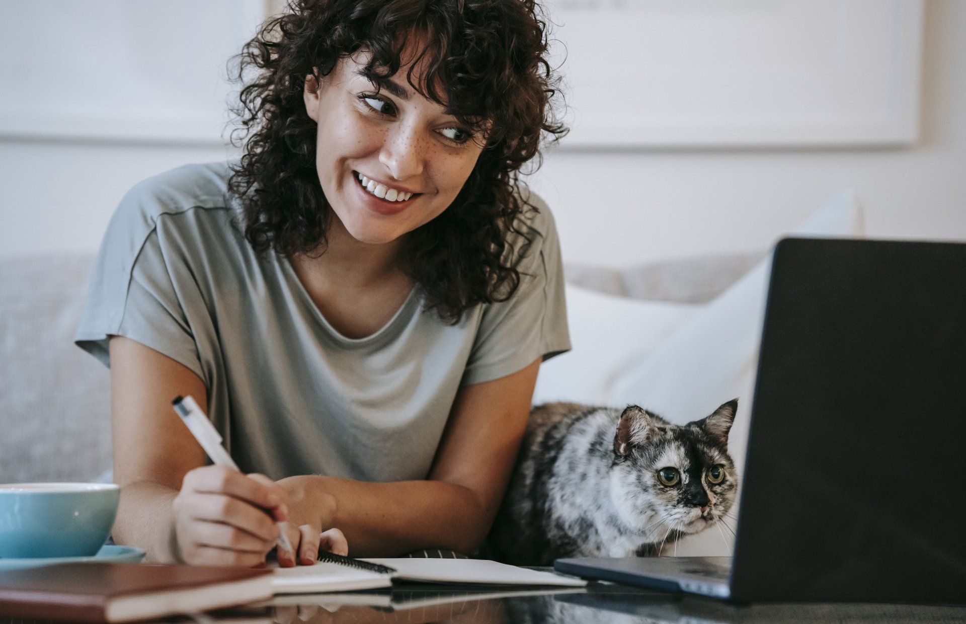 a woman is sitting at a table with a laptop and a cat .