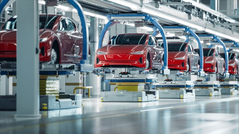 A row of red cars are sitting on a conveyor belt in a factory.