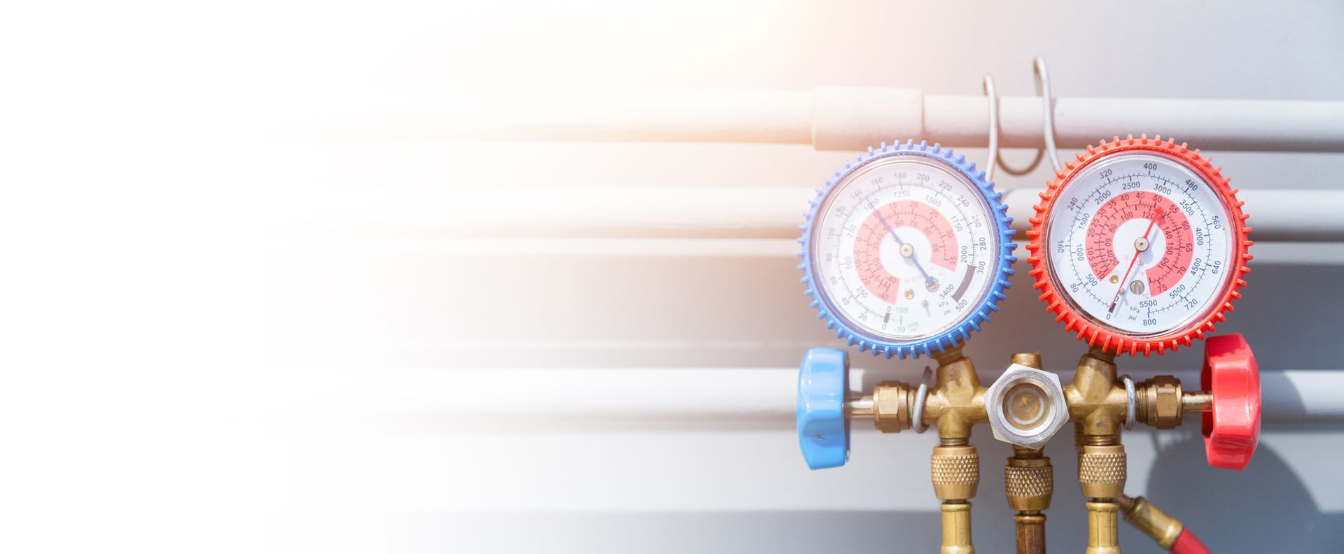 HVAC technician in yellow hard hat repairs an air conditioner unit on a ladder. Interior setting, bright.