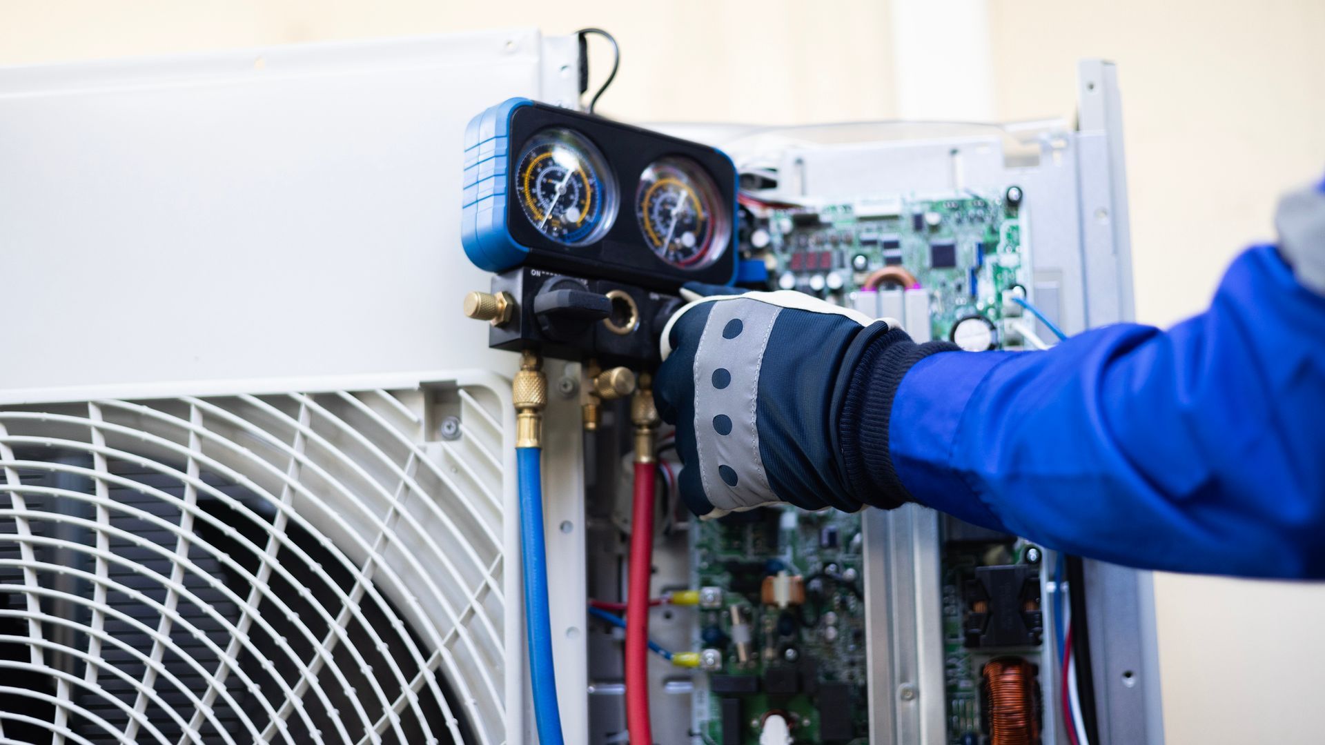 HVAC technician in blue shirt and gloves working on an air conditioning unit with gauges and hoses.