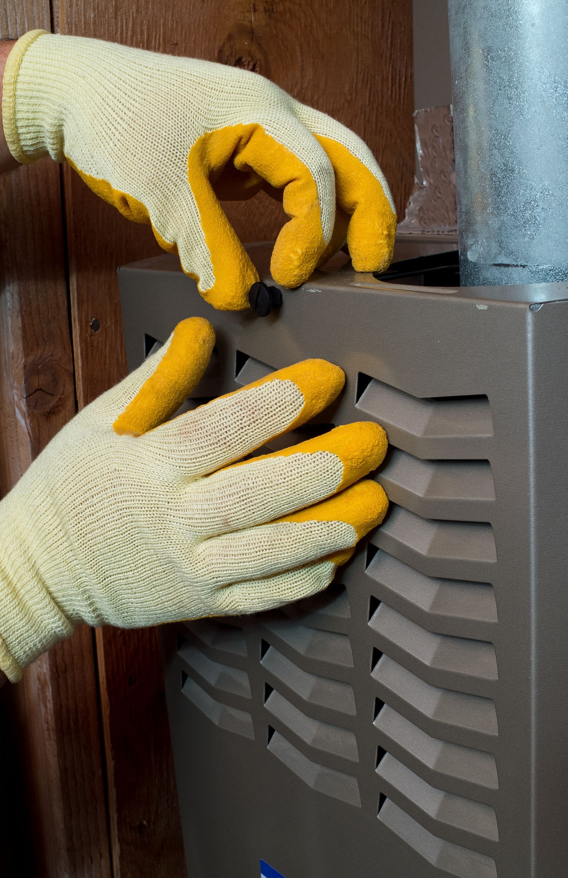 Hands in yellow gloves interacting with a brown furnace, likely changing filter.