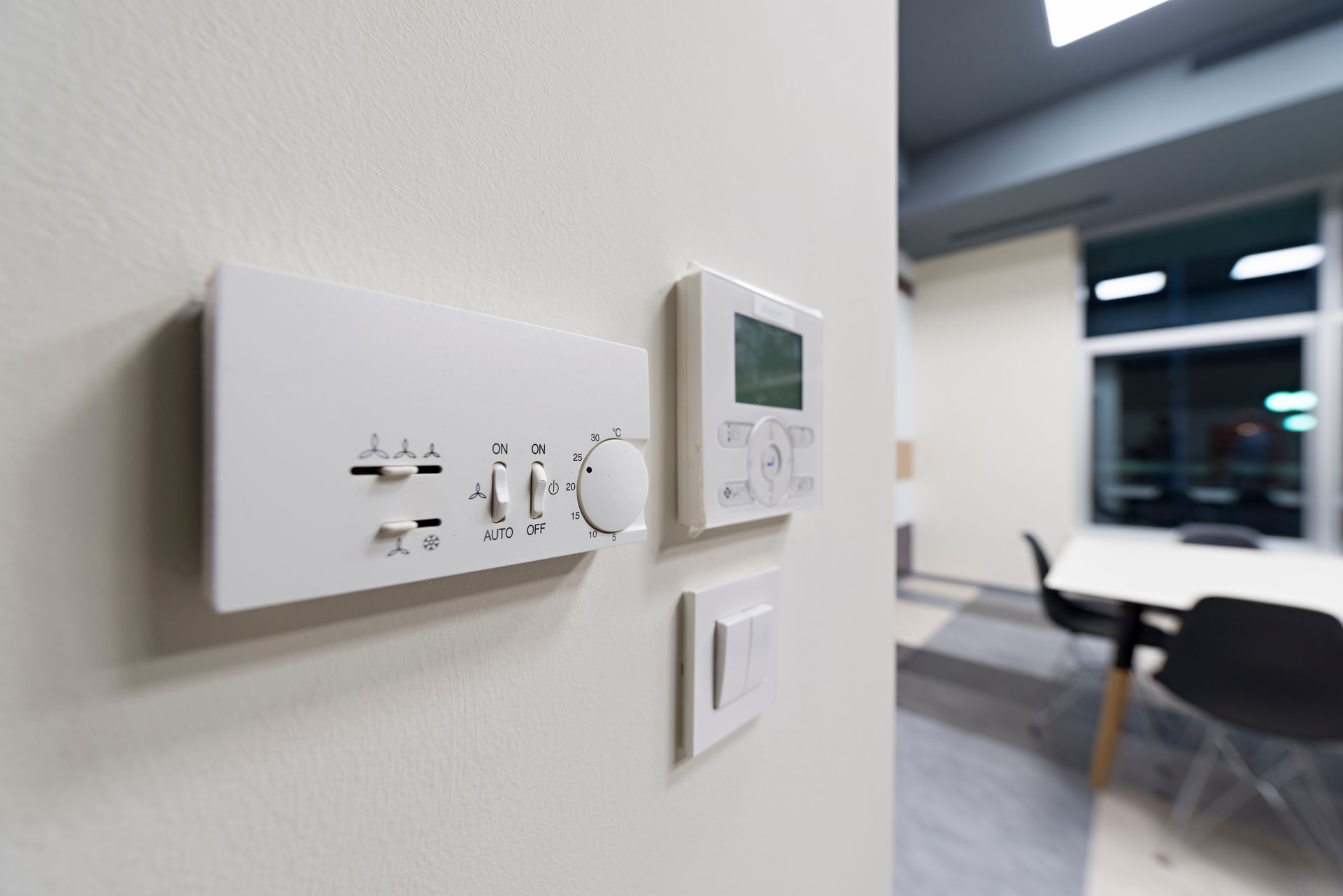 White thermostats and light switch on a wall in an office setting.