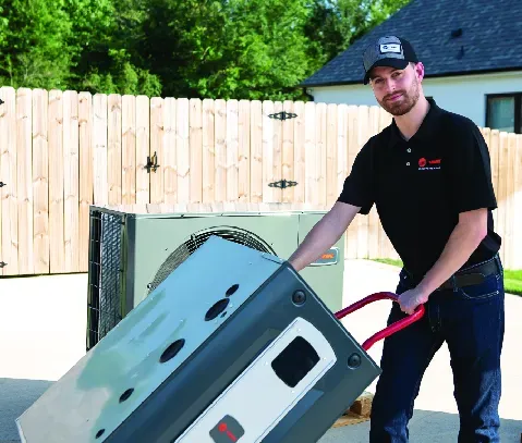 Man in uniform moves an HVAC unit on a hand truck outdoors.