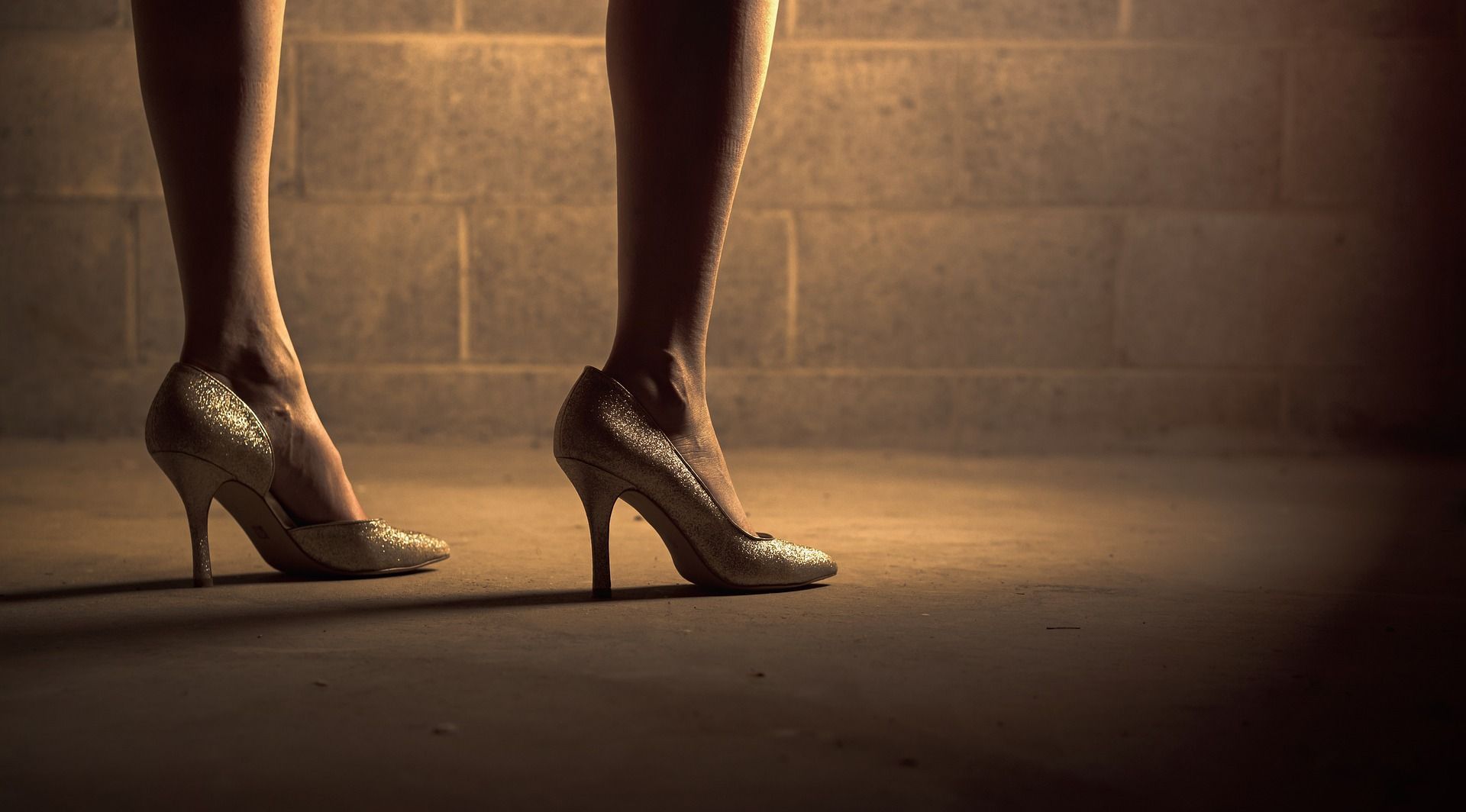 A woman wearing high heels is standing in front of a brick wall.