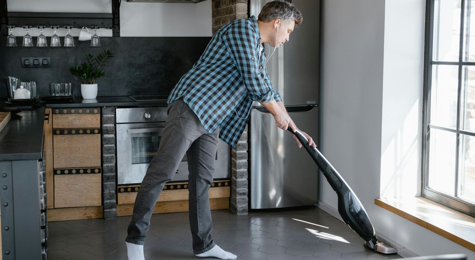 A man is cleaning the floor in a kitchen with a vacuum cleaner.