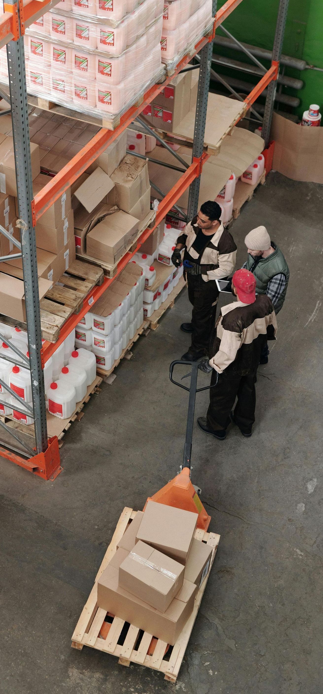 A group of people are standing in a warehouse looking at boxes on a pallet.