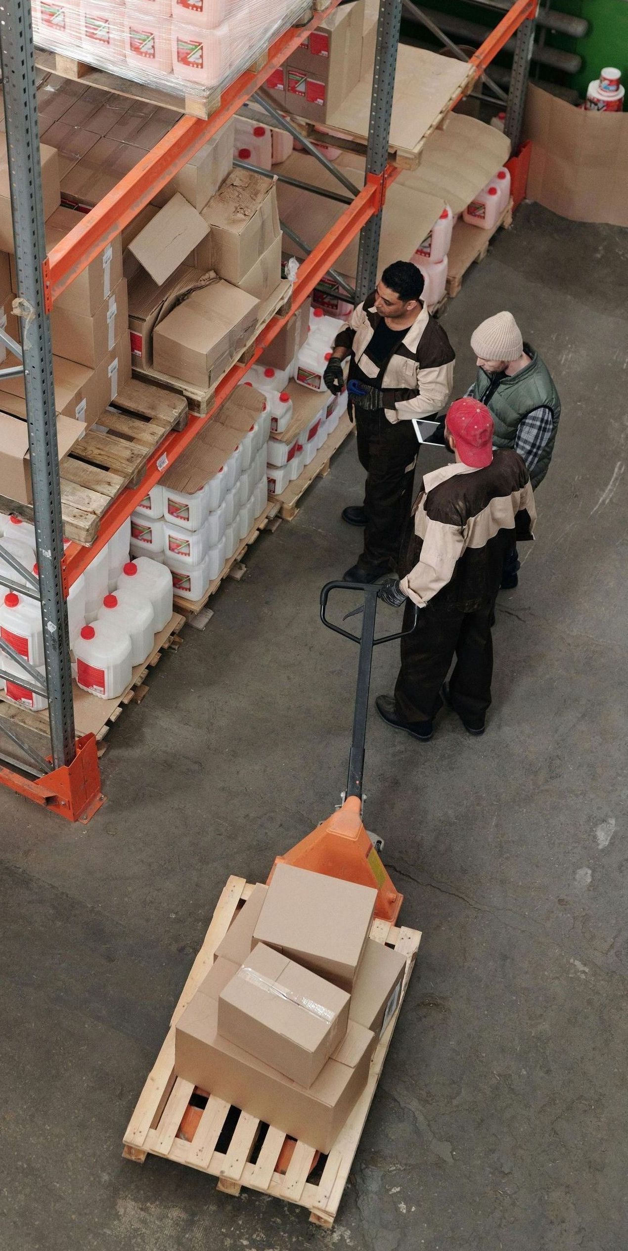 A group of people are standing around a pallet in a warehouse.