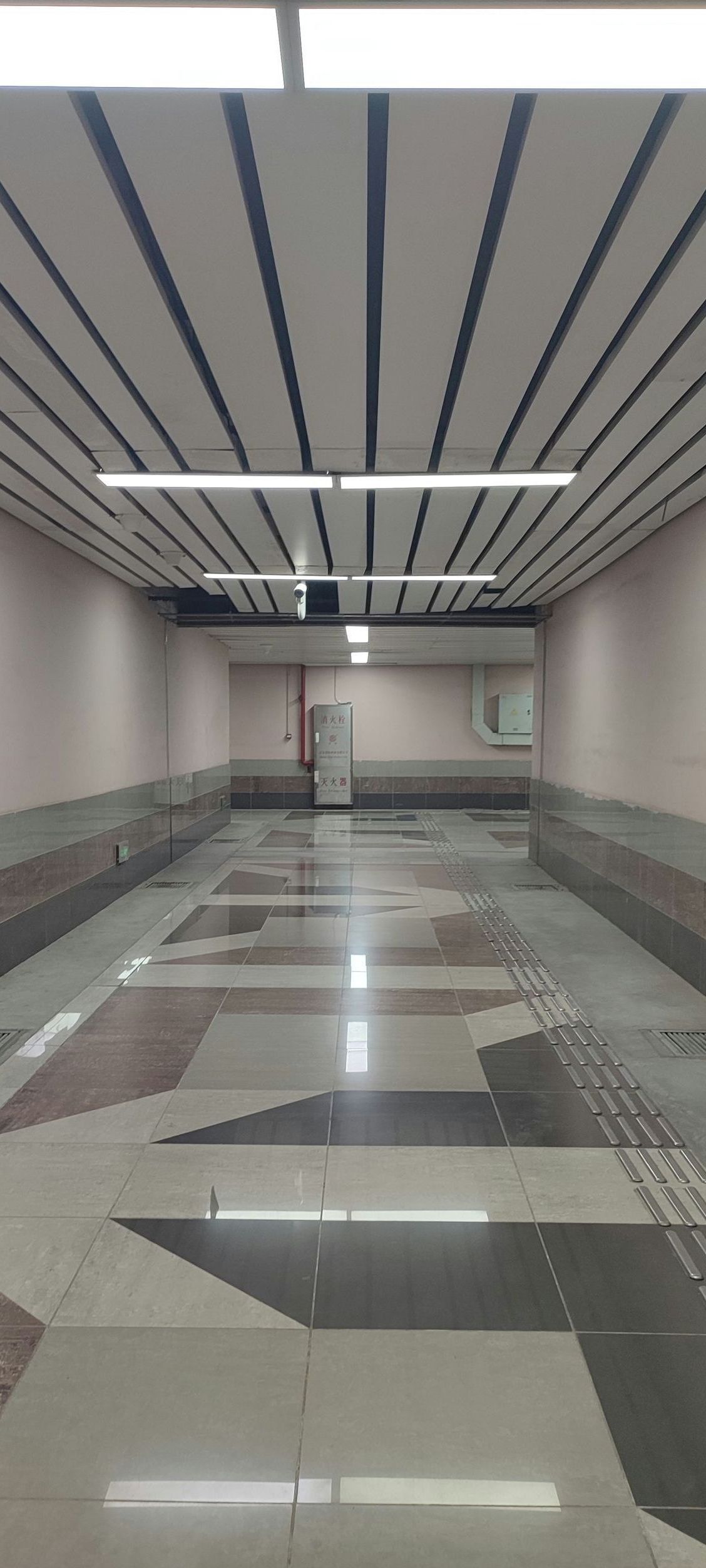 An empty subway station with a tiled floor and a striped ceiling.